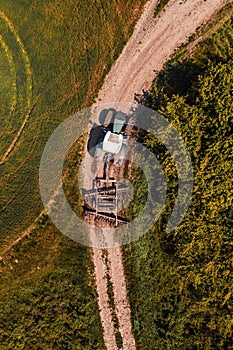 Aerial view of agricultural tractor with tiller attached on dirt road driving to the field, drone pov