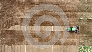 Aerial view of an agricultural tractor tilling a field creating furrows in the soil moving in a straight line from left to right