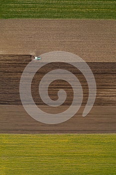 Aerial view of agricultural tractor tilling and harrowing ploughed field, directly above drone pov