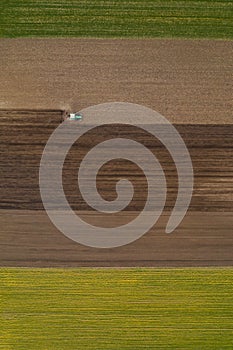 Aerial view of agricultural tractor tilling and harrowing ploughed field, directly above drone pov photo