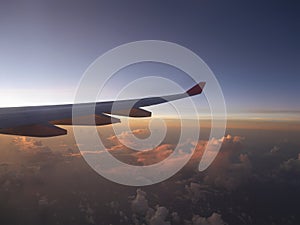 Aerial view from airplane, seeing plane`s wing and pink sunset light from left side