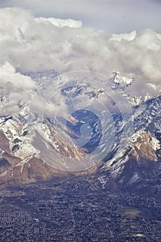 Aerial view from airplane of the Wasatch Front Rocky Mountain Range with snow capped peaks in winter including urban cities of Pro