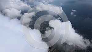 Aerial view from airplane window at high altitude of distant city covered with puffy cumulus clouds forming before