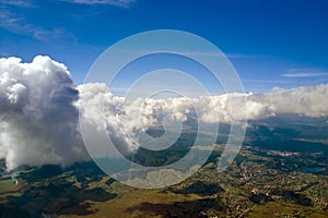 Aerial view from airplane window at high altitude of distant city covered with puffy cumulus clouds forming before rainstorm
