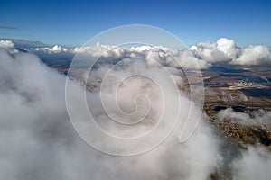 Aerial view from airplane window at high altitude of distant city covered with puffy cumulus clouds forming before
