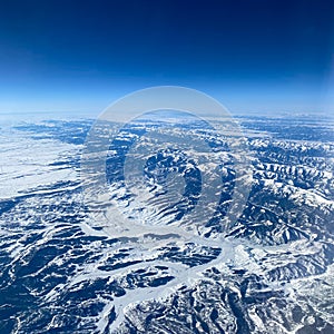 An aerial view from an airplane window of mountains, snow, clouds and blue skies