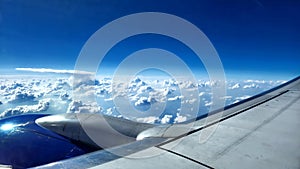 Aerial view of an airplane wing hovering above the clouds in a clear blue sky