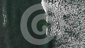 Aerial view of alone surfer at ocean and wave splashing with white foam at sunny day. Top down view of wave rolling on