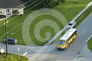 Aerial view of american yellow school bus picking up children at sidewalk bus stop for their lessongs in early morning