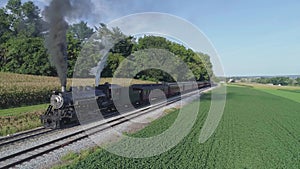 Aerial View of an Antique Restored Steam Engine Blowing Smoke with Passenger Cars pulling out of a Station