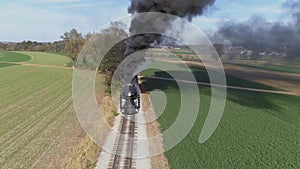 Aerial view of an antique restored steam engine in farmlands blowing black smoke