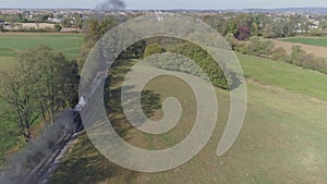 Aerial view of an antique restored steam engine in farmlands blowing black smoke with a head on view