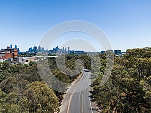 Aerial view of an asphalt city road in Melbourne skyline with forest trees under blue sky