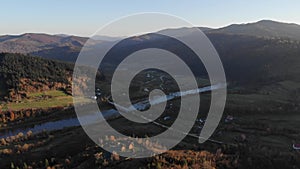 Aerial view of autumn landscape: mountains, forests and river. Cozy wooden country houses on the slopes. Carpathian Mountains in U