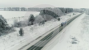 Aerial view of a b freight truck driving down a highway running along a railroad on a clear winter day. Cargo trucks