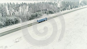 Aerial view of a b freight truck driving down a highway running along a railroad on a clear winter day. Cargo trucks