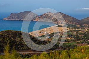 Aerial view of a beach and people enjoying a sunny day, with a forested mountain in the background