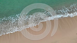 Aerial view of beach with turquoise clear ocean water and white sand beach. Small white foam waves rolling to coast