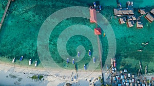 Aerial view of a beach with white sand and clear water with a boardwalk to a dock