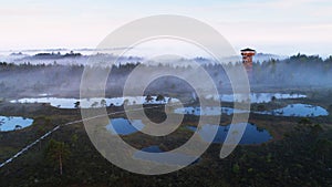 An aerial view of beautiful bog in Estonian nature during foggy sunrise with a watching tower and hiking trail, Northern Eu