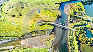 Aerial view on a beautiful bridge across a small river surrounded by green meadow. Taranaki region, New Zealand