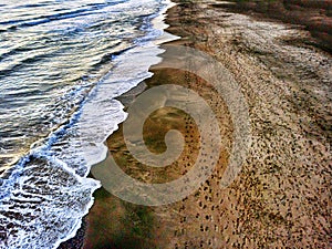 Aerial view of a beautiful coastline and undertow with footsteps on the sand photo