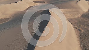 Aerial view - a beautiful girl standing on a dune at sunset or sunrise. Flying drone at high speed over the desert - a