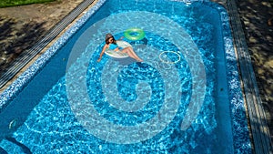 Aerial view of beautiful girl in swimming pool from above, swim on inflatable ring donut and has fun in water on family vacation