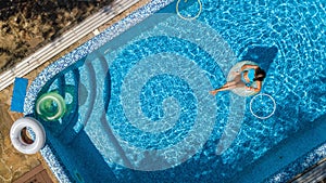 Aerial view of beautiful girl in swimming pool from above, swim on inflatable ring donut and has fun in water on family vacation