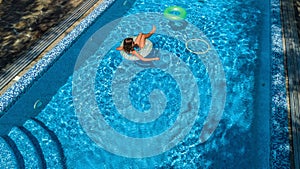 Aerial view of beautiful girl in swimming pool from above, swim on inflatable ring donut and has fun in water on family vacation