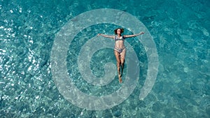 Aerial view of beautiful happy woman in swimsuit laying in the shallow sea water enjoying beach and soft turquoise ocean wave.