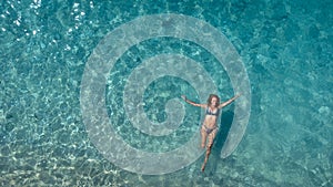 Aerial view of beautiful happy woman in swimsuit laying in the shallow sea water enjoying beach and soft turquoise ocean wave.