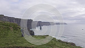Aerial view of beautiful irish cliffs, young couple watch the landscape, panorama. Cloudy sky in the background, rough