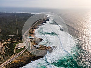 Aerial view of a beautiful isolated road with vehicles driving along south Portuguese coastline facing the Atlantic Ocean rough