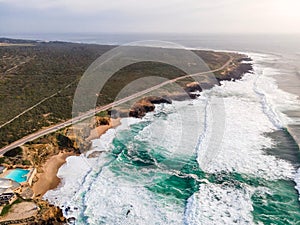 Aerial view of a beautiful isolated road with vehicles driving along south Portuguese coastline facing the Atlantic Ocean rough