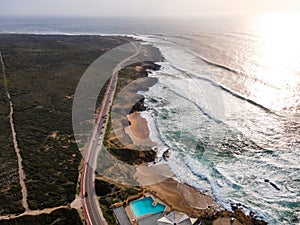 Aerial view of a beautiful isolated road with vehicles driving along south Portuguese coastline facing the Atlantic Ocean rough