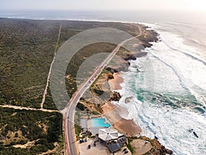 Aerial view of a beautiful isolated road with vehicles driving along south Portuguese coastline facing the Atlantic Ocean rough