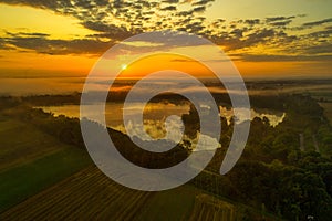 Aerial view of a beautiful lake at early sunrise with foggy trees surrounded