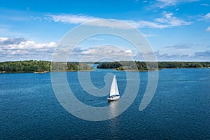 Aerial view of beautiful modern white sailing yacht sails on the sea surface on sunny summer day. Shot from cruise ship. Forest