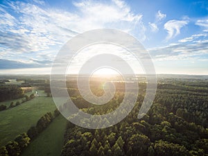 Aerial view of a beautiful sunset over rural landscape with forests and green fields