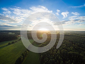 Aerial view of a beautiful sunset over rural landscape with forests and green fields