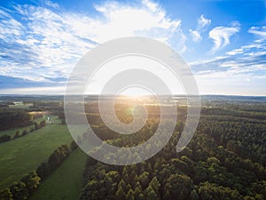 Aerial view of a beautiful sunset over rural landscape with forests and green fields