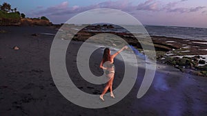 Aerial  view of beautiful woman in bikini dancing with colored smoke at the black sand beach at sunset