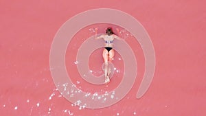 Aerial view. A beautiful young girl lies on in the pink lake, a bikini, sunglasses, pink clear water, a top view