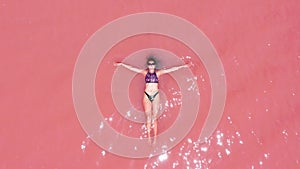 Aerial view. A beautiful young girl lies on in the pink lake, a bikini, sunglasses, pink clear water, a top view