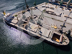 Aerial view of big cargo ship bulk carrier is loaded with grain of wheat in port at sunny day