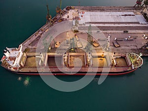 Aerial view of big cargo ship bulk carrier is loaded with grain of wheat in port at sunset