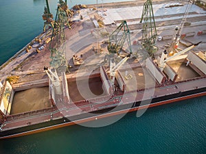 Aerial view of big cargo ship bulk carrier is loaded with grain of wheat in port at sunset