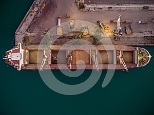 Aerial view of big cargo ship bulk carrier is loaded with grain of wheat in port at sunset