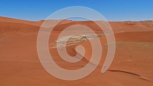 Aerial view of big orange sand dunes with two people walking in the valley at Sossusvlei, Namib desert, Namibia, Africa.
